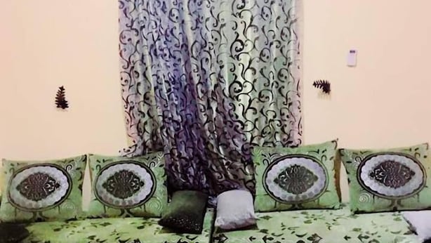 Une pièce avec un canapé vert, des rideaux à motifs et un revêtement de sol décoratif.