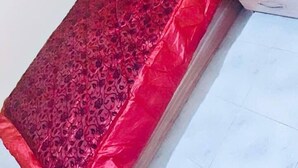 Un lit simple avec une couvre-lit rouge et des coussins assortis, placé contre un mur blanc dont le sol est recouvert de carreaux.