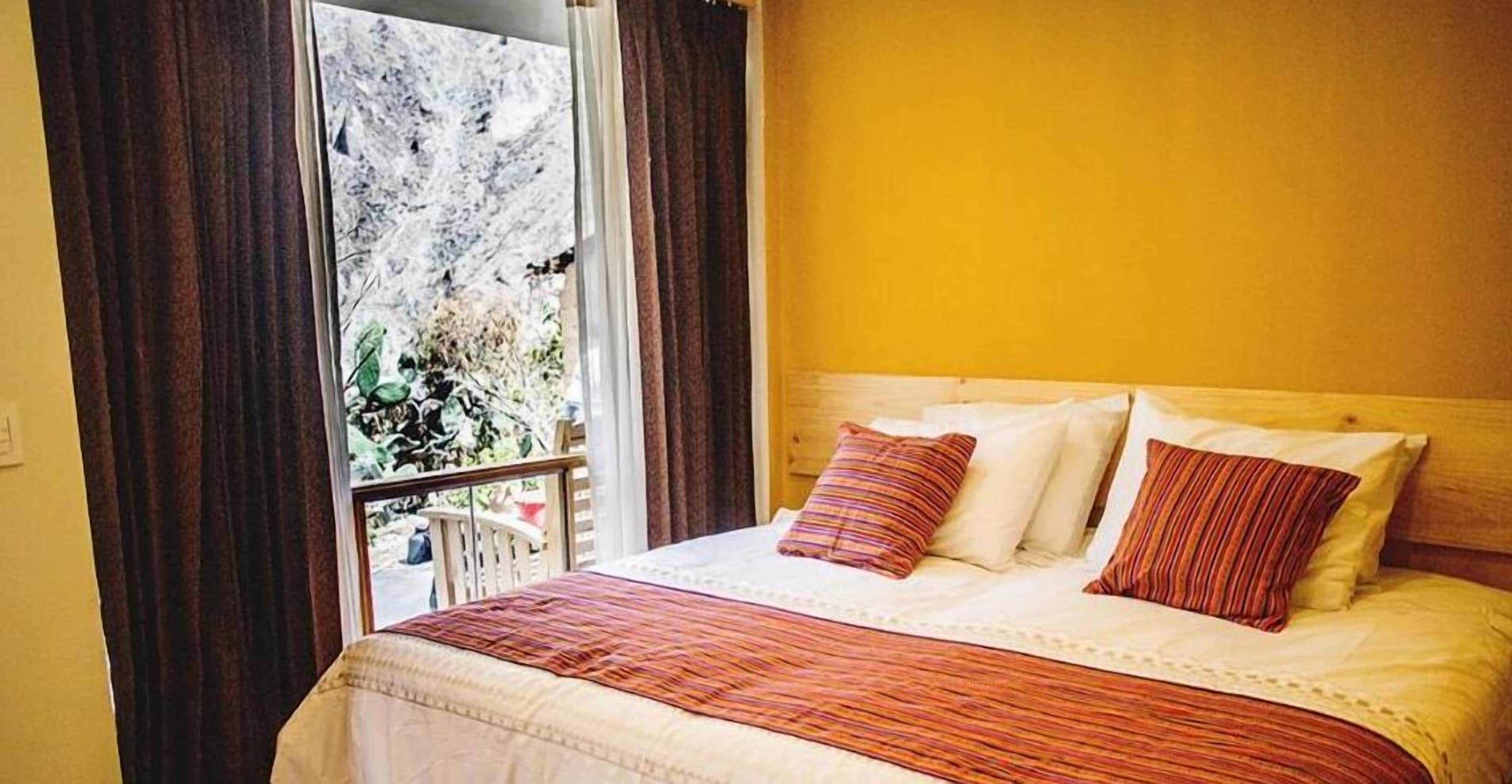 A bedroom with a bed, curtains, and a window with a view of greenery.