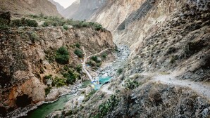 A canyon with a river, rocky terrain, and a small bridge. - Colibrí Lodge (Tapay)