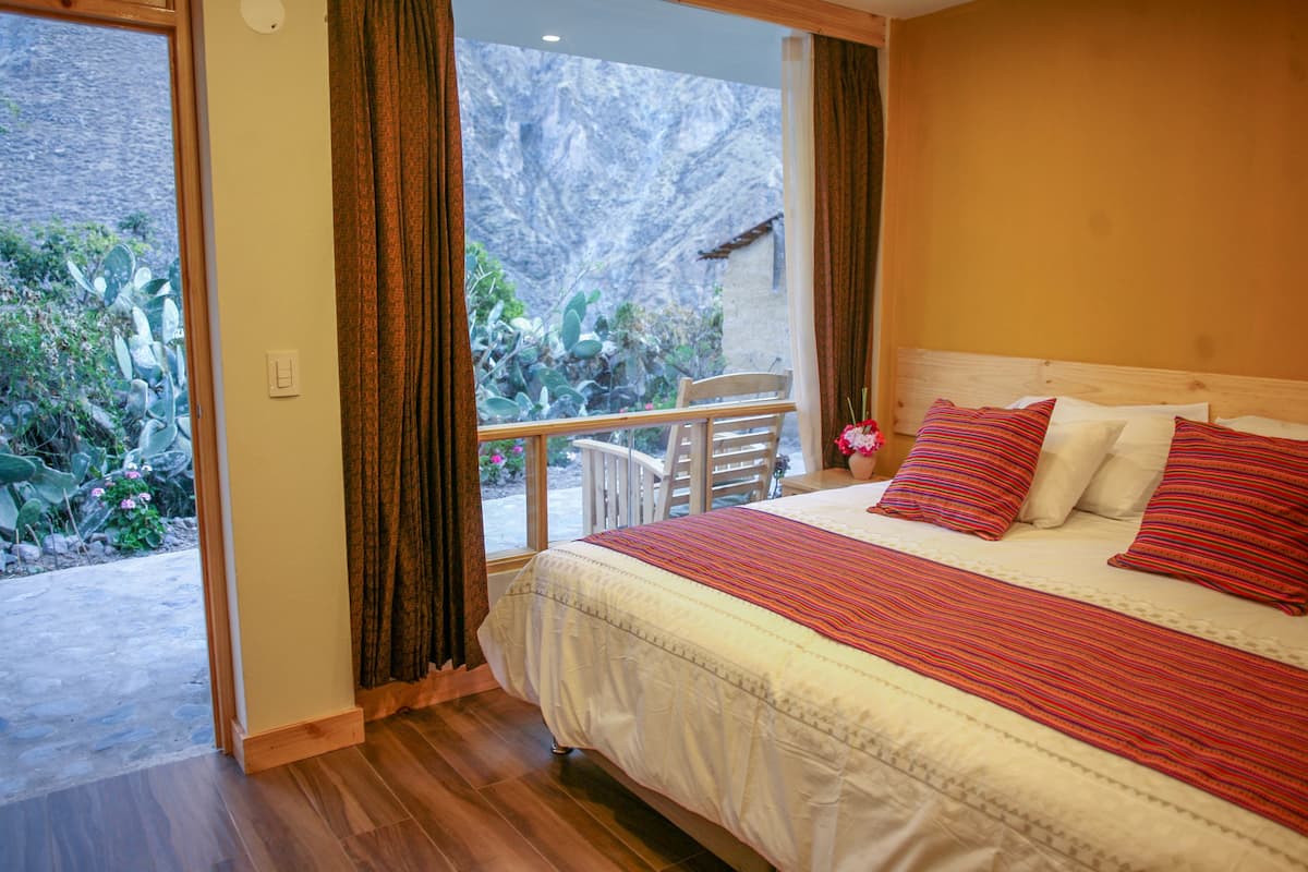 Un dormitorio con una cama grande, un balcón con vistas a cactus y flores, y suelo de madera.