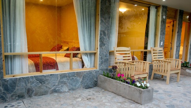 A room with a bed, wooden chairs, and a window with curtains. - Colibrí Lodge (Tapay)
