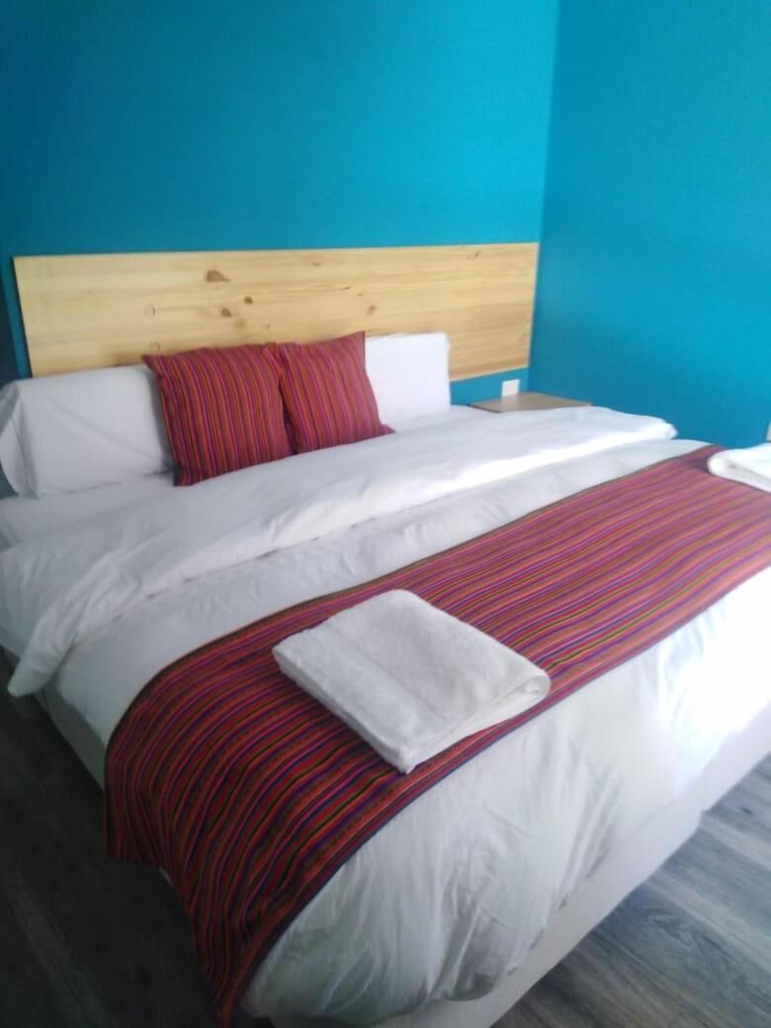 Una cama con cabecera de madera, ropa de cama blanca y una manta a rayas rojas.