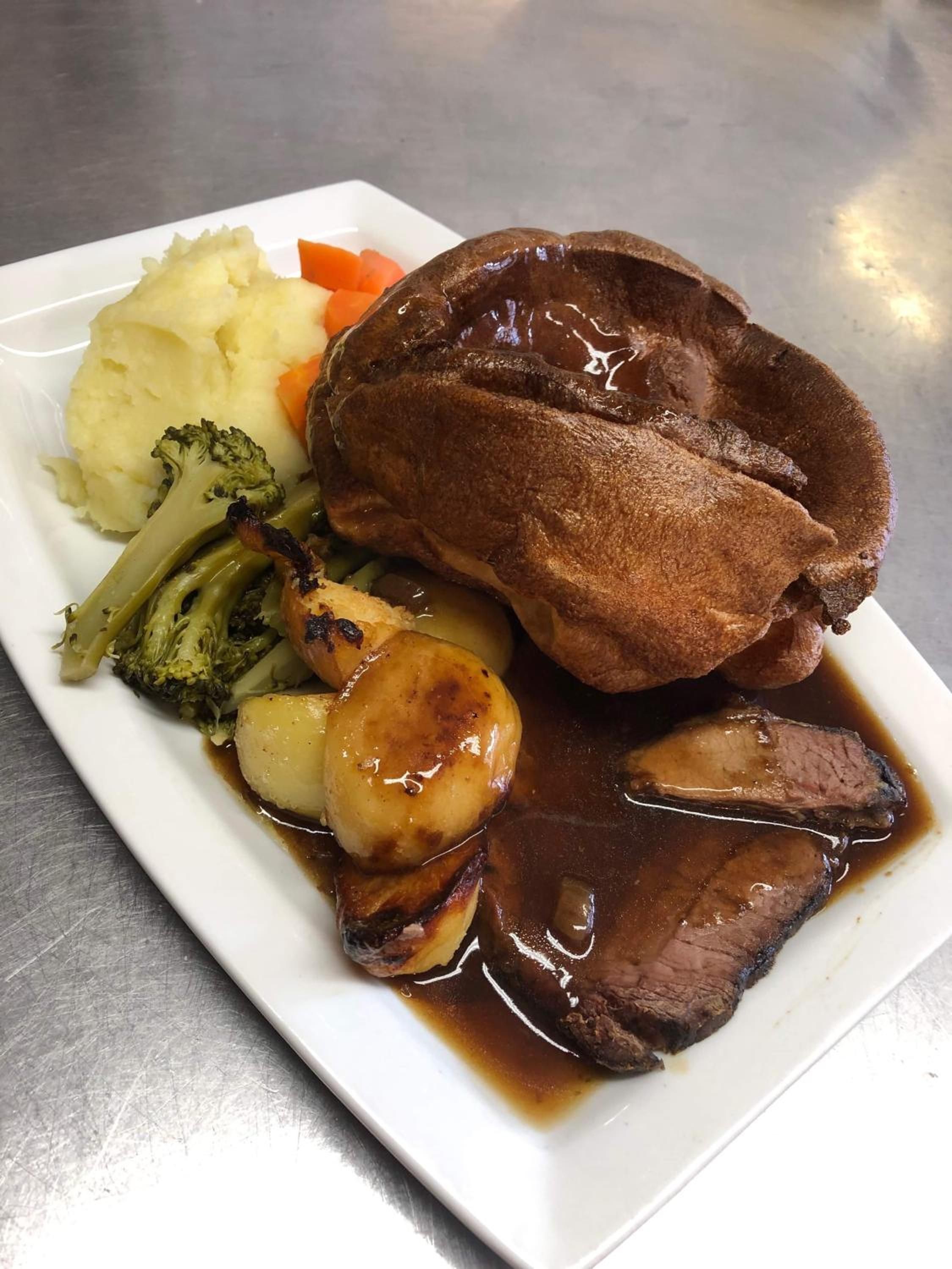 A plate of food with roast beef, Yorkshire pudding, mashed potatoes, and vegetables.
