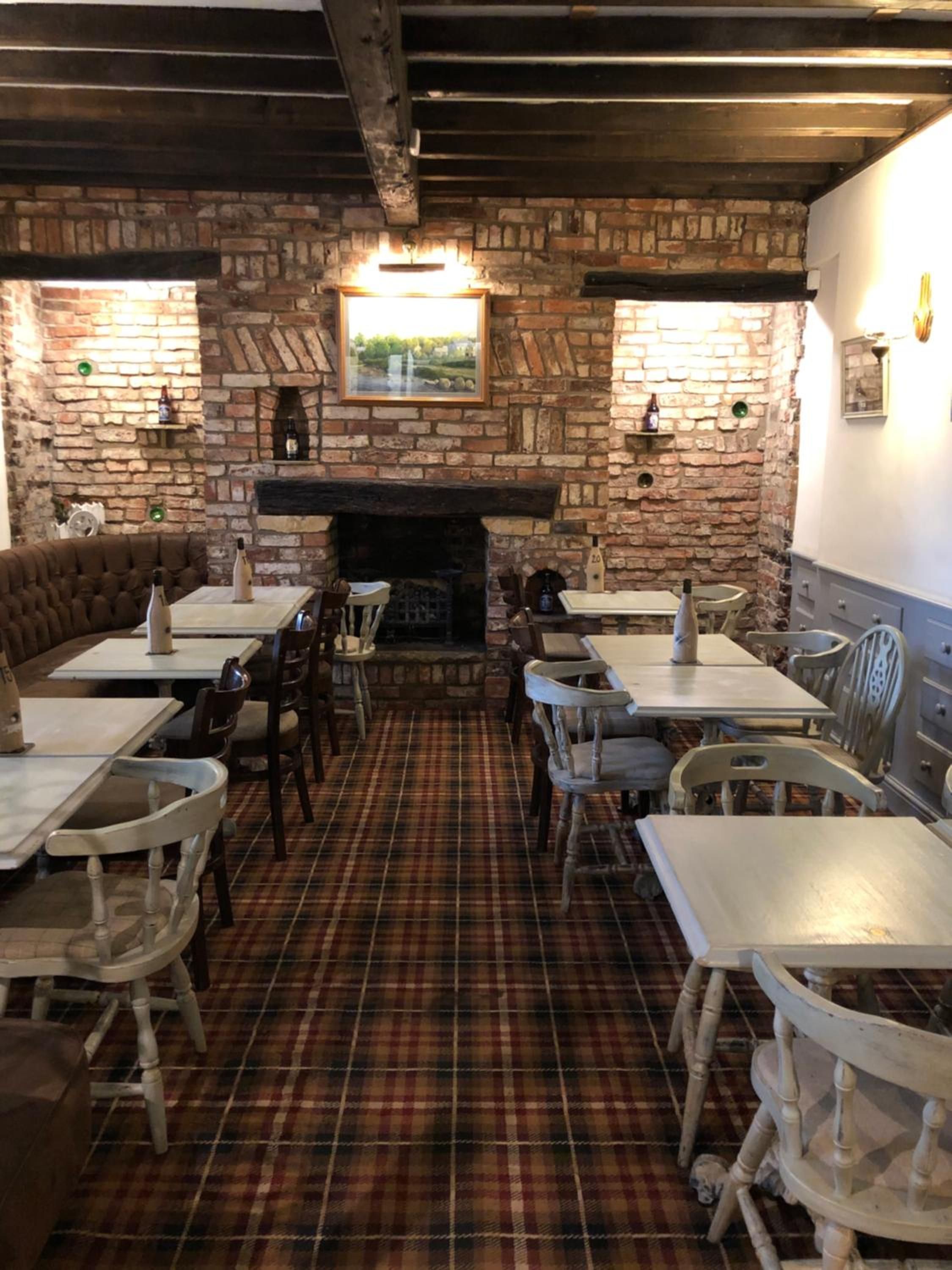 A pub with a brick fireplace, wooden furniture, and a plaid floor.