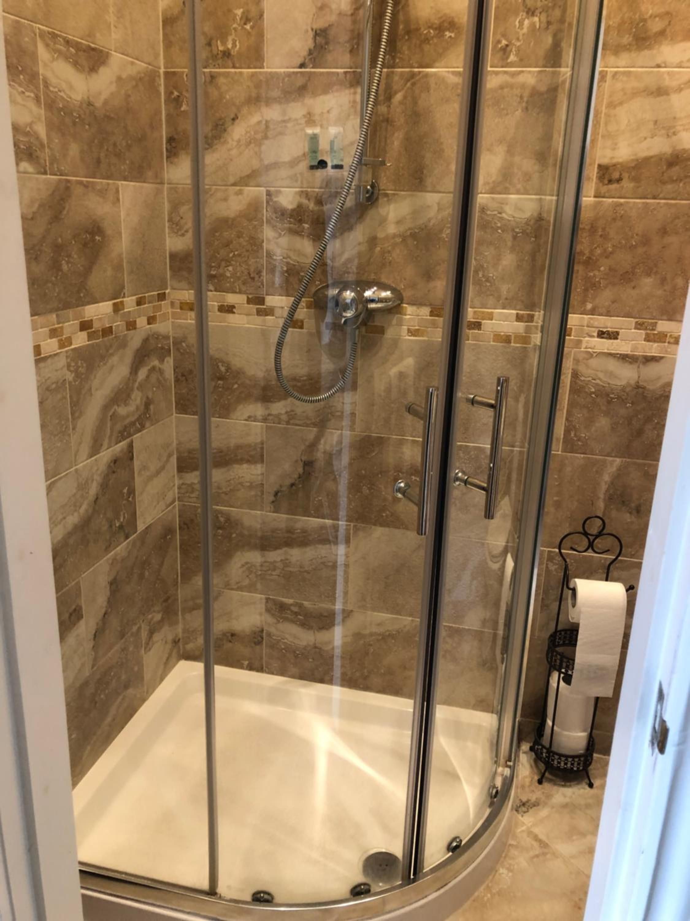Cabina de ducha con paredes de vidrio, cabezal de ducha de mano y grifo empotrado.
