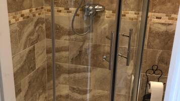 Cabina de ducha con paredes de vidrio, cabezal de ducha de mano y grifo empotrado.