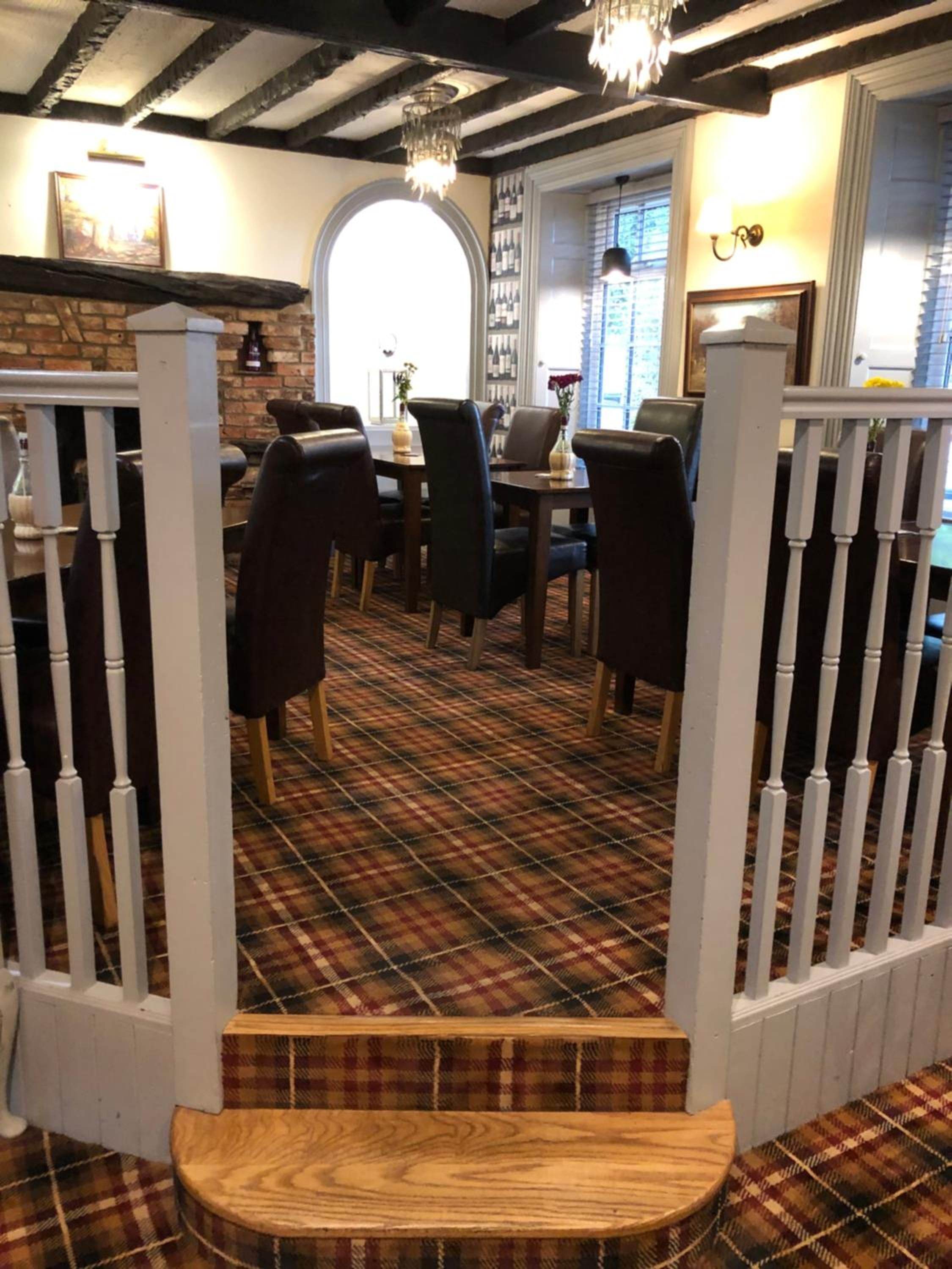 A dining area with a checkered floor, wooden chairs, a table, and a staircase leading to a higher level.