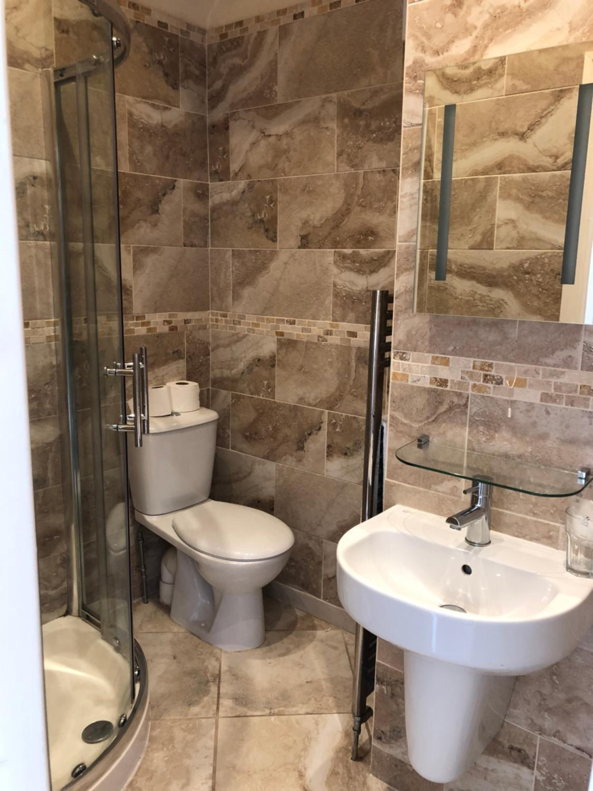 A bathroom with a glass shower enclosure, a toilet, a sink, and a mirror.