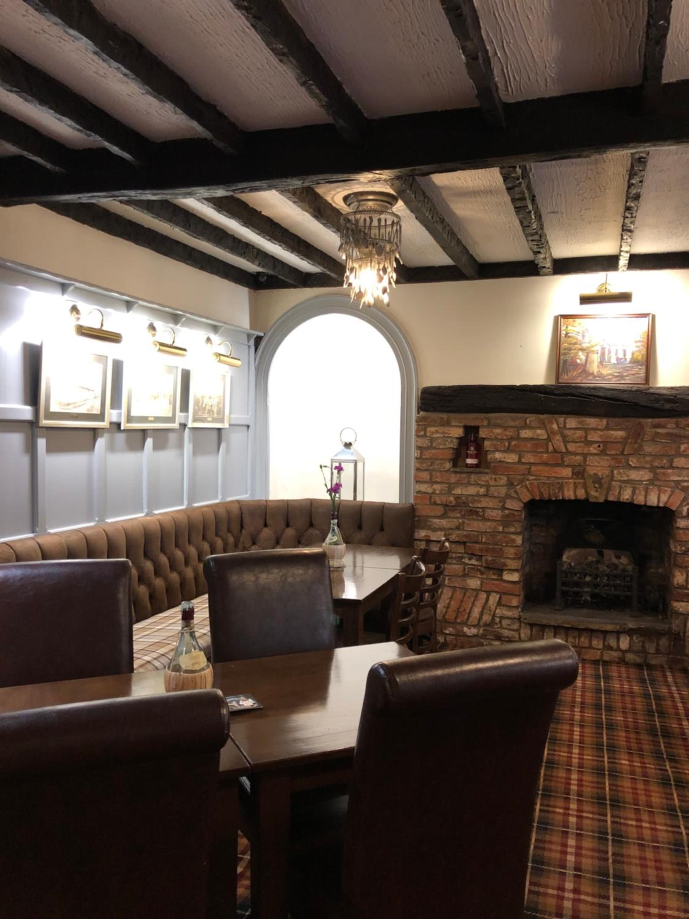 A restaurant interior with a stone fireplace, wooden ceiling beams, and a bench seating area.