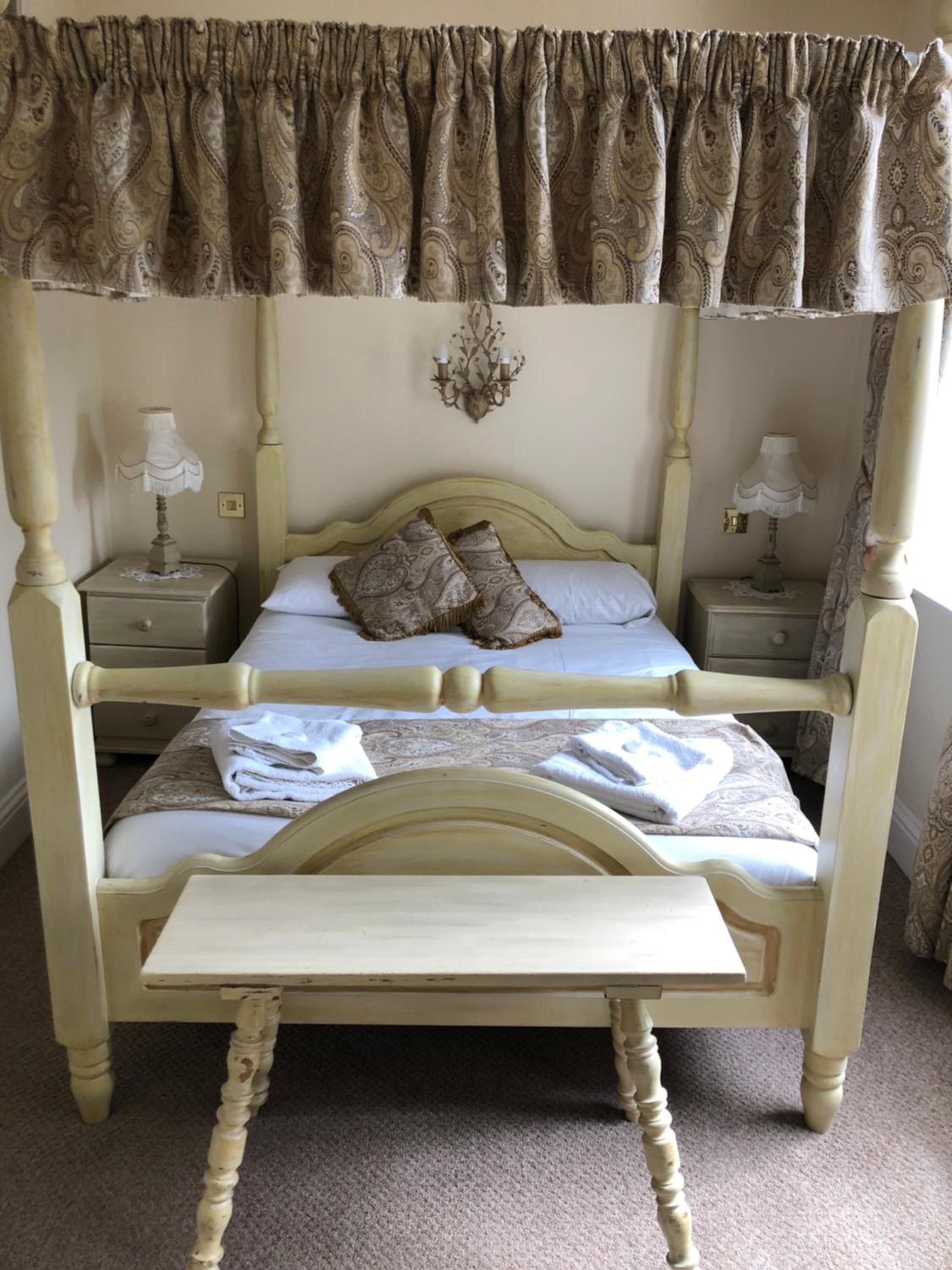 A double bed with a canopy, two bedside tables with lamps, and a small table in front of the bed.