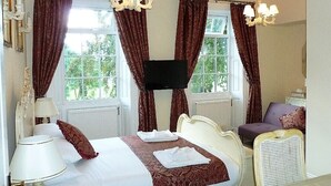 Ein Hotelzimmer mit einem großen Bett, einem Fernseher, einem Sessel und Vorhängen.
