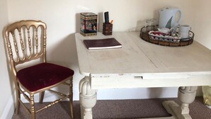 Une pièce comprenant une chaise en bois avec un siège rembourré, une table blanche sur laquelle se trouve un plateau avec une théière, des tasses et un livre.