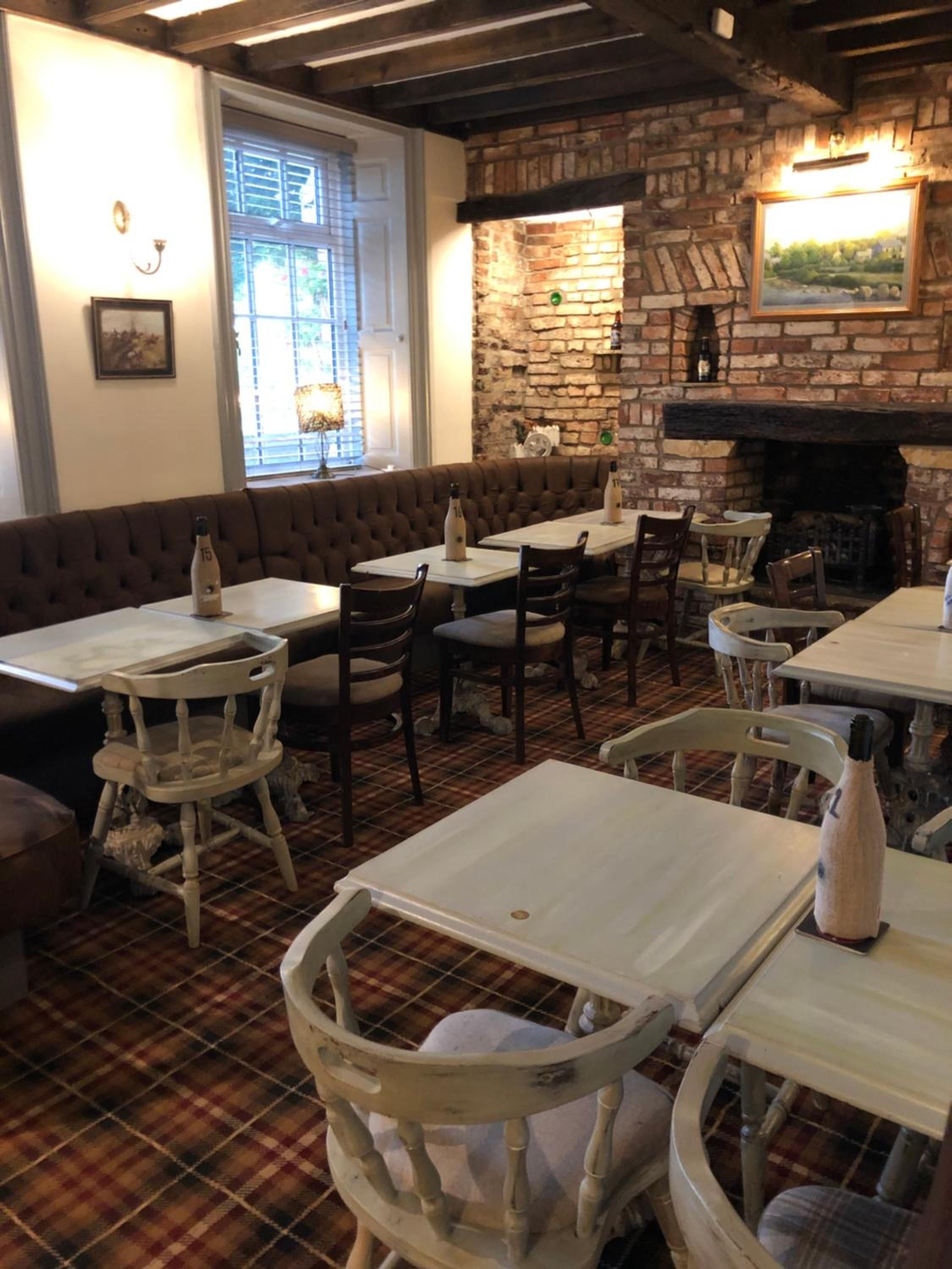 A restaurant interior with brick walls, a fireplace, and a plaid floor. Tables and chairs are arranged for dining.