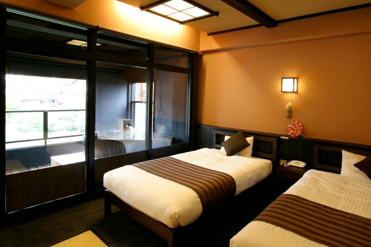 A hotel room with two beds, a large window, and a nightstand with a phone.