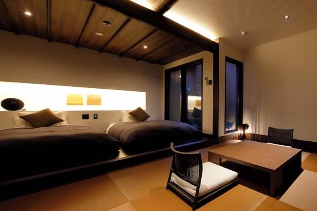 A modern hotel room with a bed, bedside tables, a chair, and a large window.