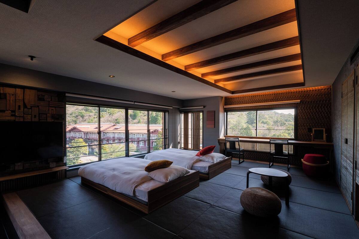 A modern hotel room with a large bed, a TV, a small table, and a view of the outside.