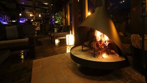 A cozy lounge area with a central fire feature, comfortable seating, and a well-lit ambiance. - Unzen Fukudaya (Unzen)