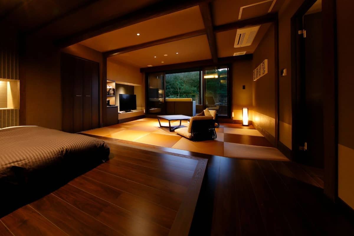 A modern hotel room with a bed, a desk, a chair, and a view of the outdoors.