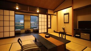 A traditional Japanese room with tatami flooring, a low table, a sofa, and a TV. - Unzen Fukudaya (Unzen)