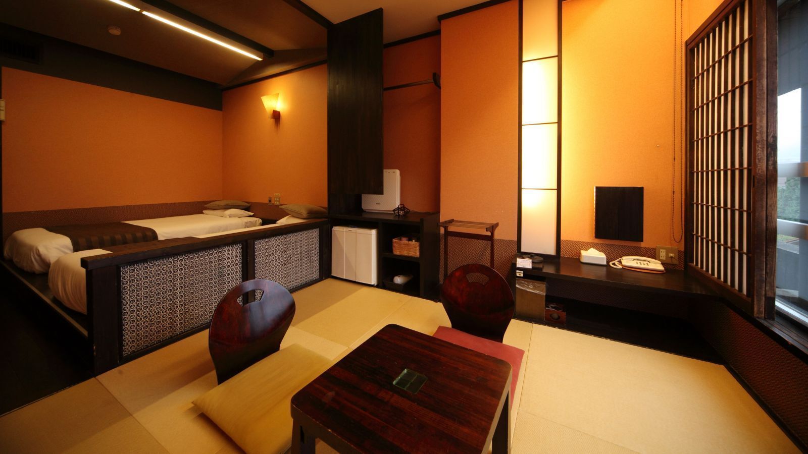 A traditional Japanese-style room with tatami flooring, a low table, a sofa, and a small kitchenette.
