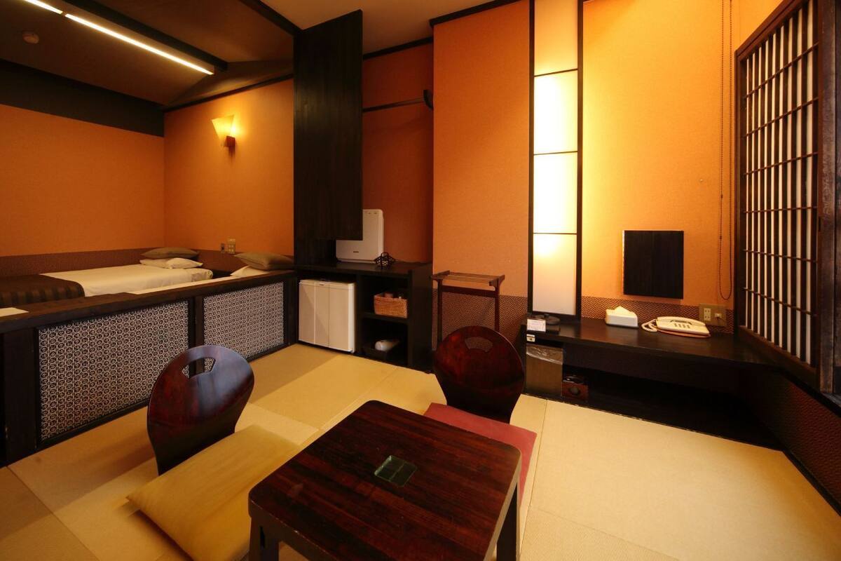 A traditional Japanese-style room with tatami flooring, a low table, a sofa, and a small kitchenette.