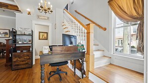A hotel room with a wooden desk, a computer, a chandelier, a staircase, and a window with curtains. - Carriage Way Centennial (St. Augustine)