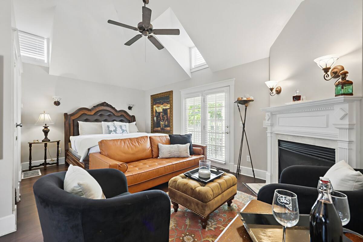 A spacious bedroom with a large bed, a leather sofa, a black armchair, and a fireplace.