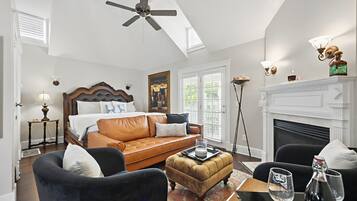 A spacious bedroom with a large bed, a leather sofa, a black armchair, and a fireplace.