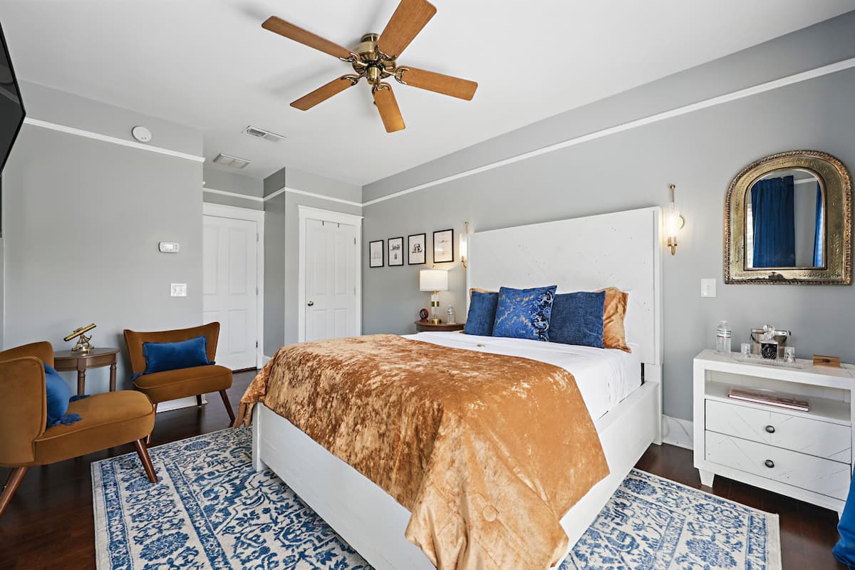 A bedroom with a large bed, a ceiling fan, a nightstand, and a dresser.