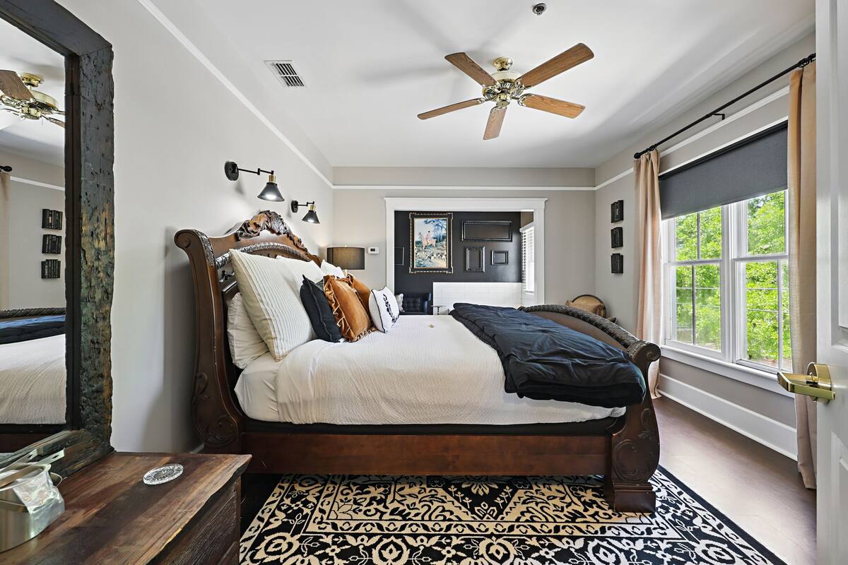 A bedroom with a large bed, a ceiling fan, a window with curtains, and a patterned rug.