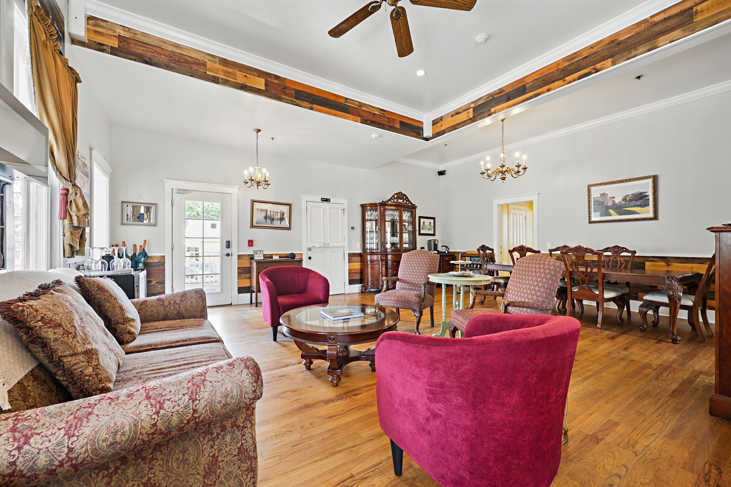 A spacious living room with a wooden ceiling, a large sofa, a red armchair, and a dining area with wooden furniture.