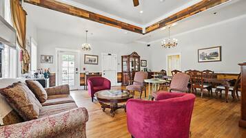 A spacious living room with a wooden ceiling, a large sofa, a red armchair, and a dining area with wooden furniture.