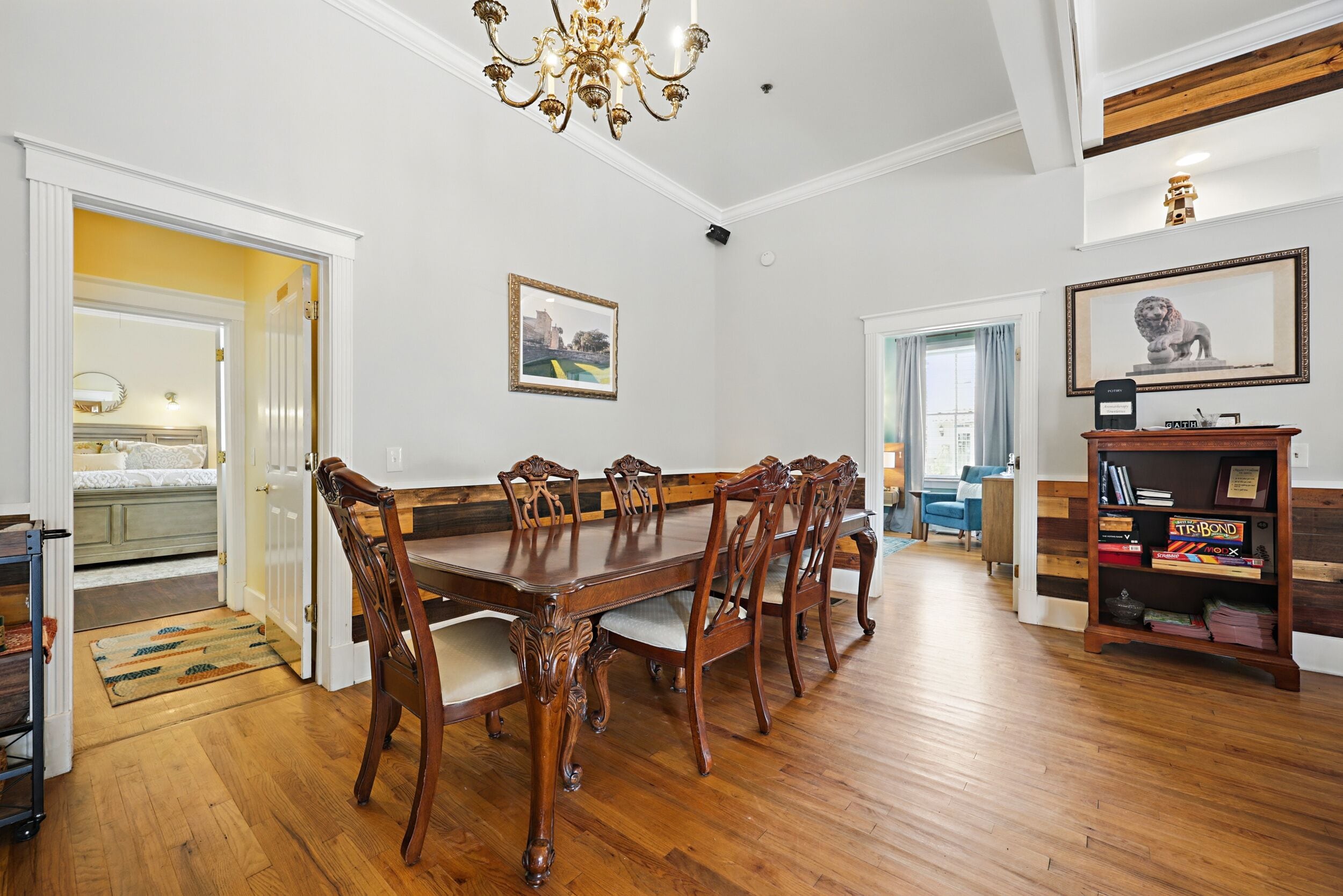 A dining area with a wooden table and chairs, a chandelier, and a bookshelf with books.