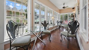 A spacious room with large windows, a glass table, and ornate chairs. - Carriage Way Centennial (St. Augustine)