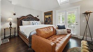 A bedroom with a large bed, a leather sofa, a bedside table, and a floor lamp. - Carriage Way Centennial (St. Augustine)