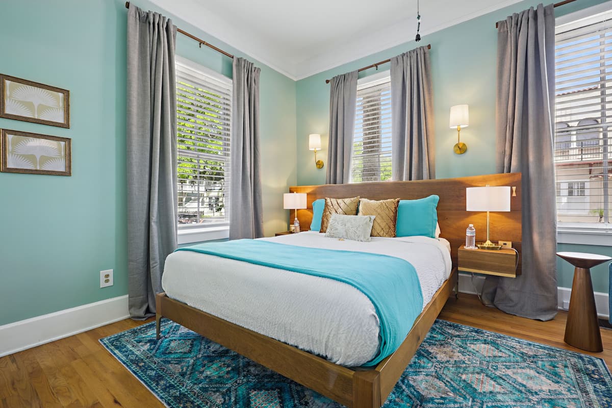 A bedroom with a large bed, two bedside tables, a nightstand, and a window with blinds.