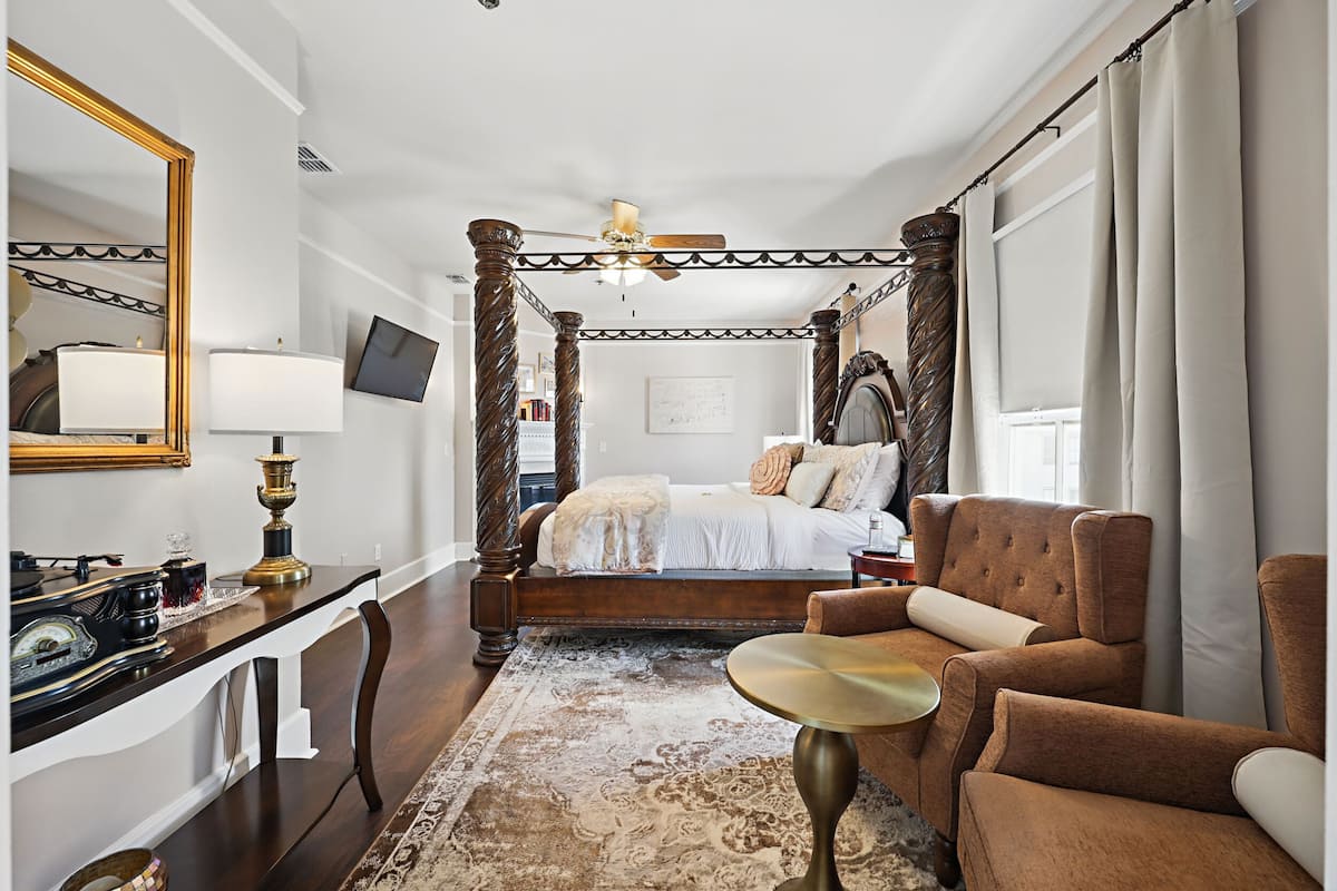 A bedroom with a four-poster bed, a desk with a lamp, a chair, and a television.