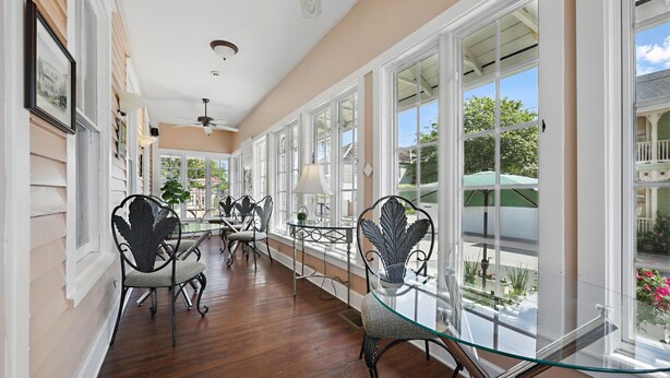 A hallway with large windows, wooden floors, and metal chairs with glass tops. - Carriage Way Centennial (St. Augustine)