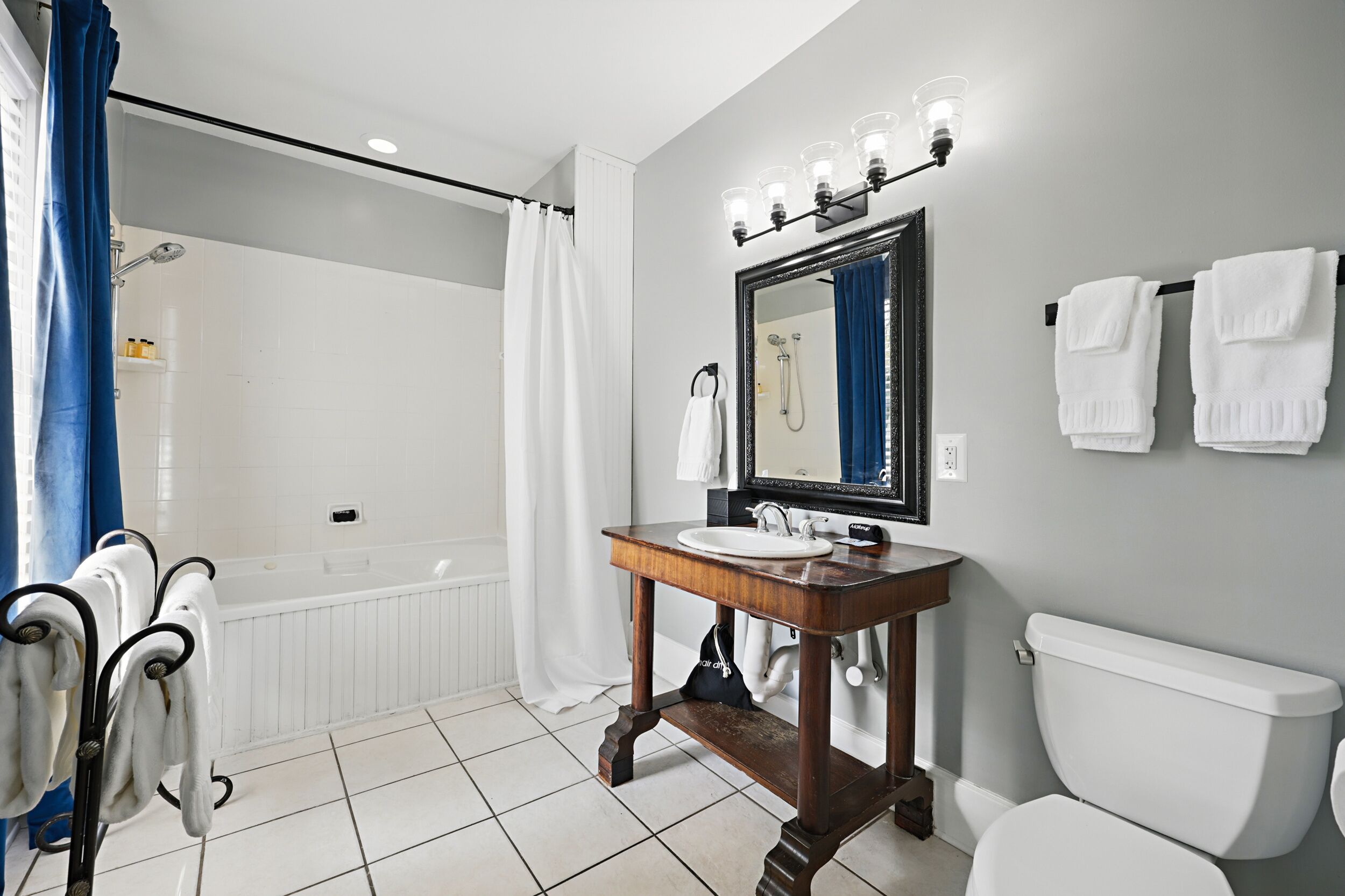 A bathroom with a white bathtub, a wooden vanity with a sink, a toilet, and a mirror with lights.