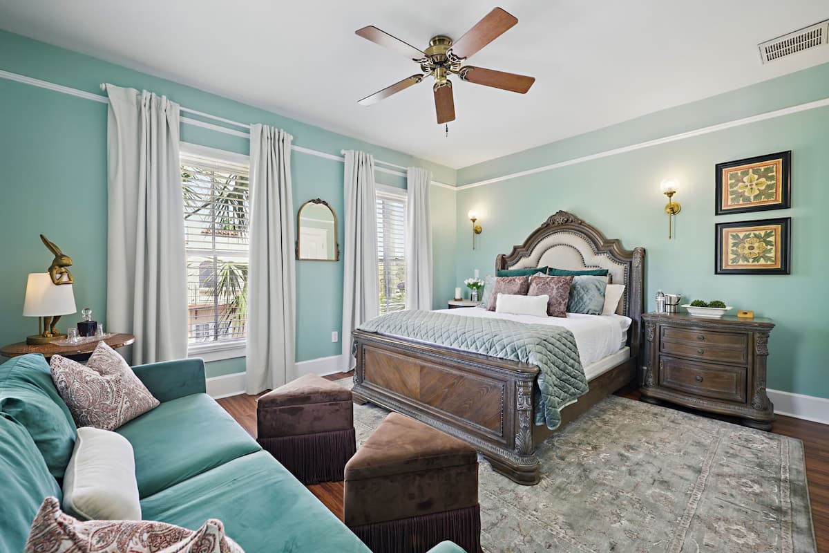 A bedroom with a bed, a sofa, a nightstand, a ceiling fan, and a window with curtains.