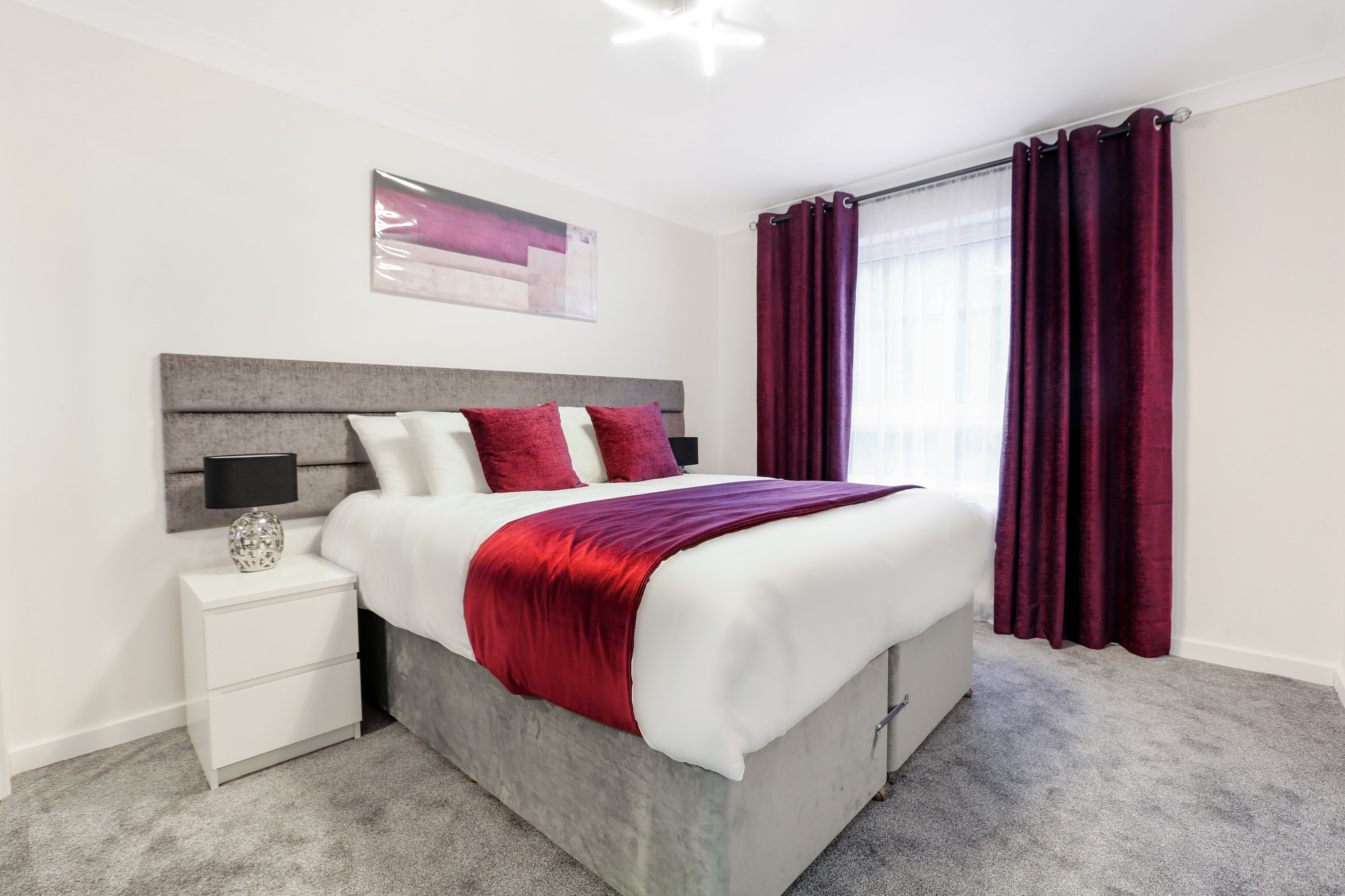 Ein modernes Schlafzimmer mit grauem Kopfteil, weißer Bettwäsche und einer roten Decke.