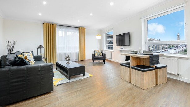 Een moderne woonkamer met een zwarte bank, een houten salontafel en een eetgedeelte met een houten tafel en stoelen.