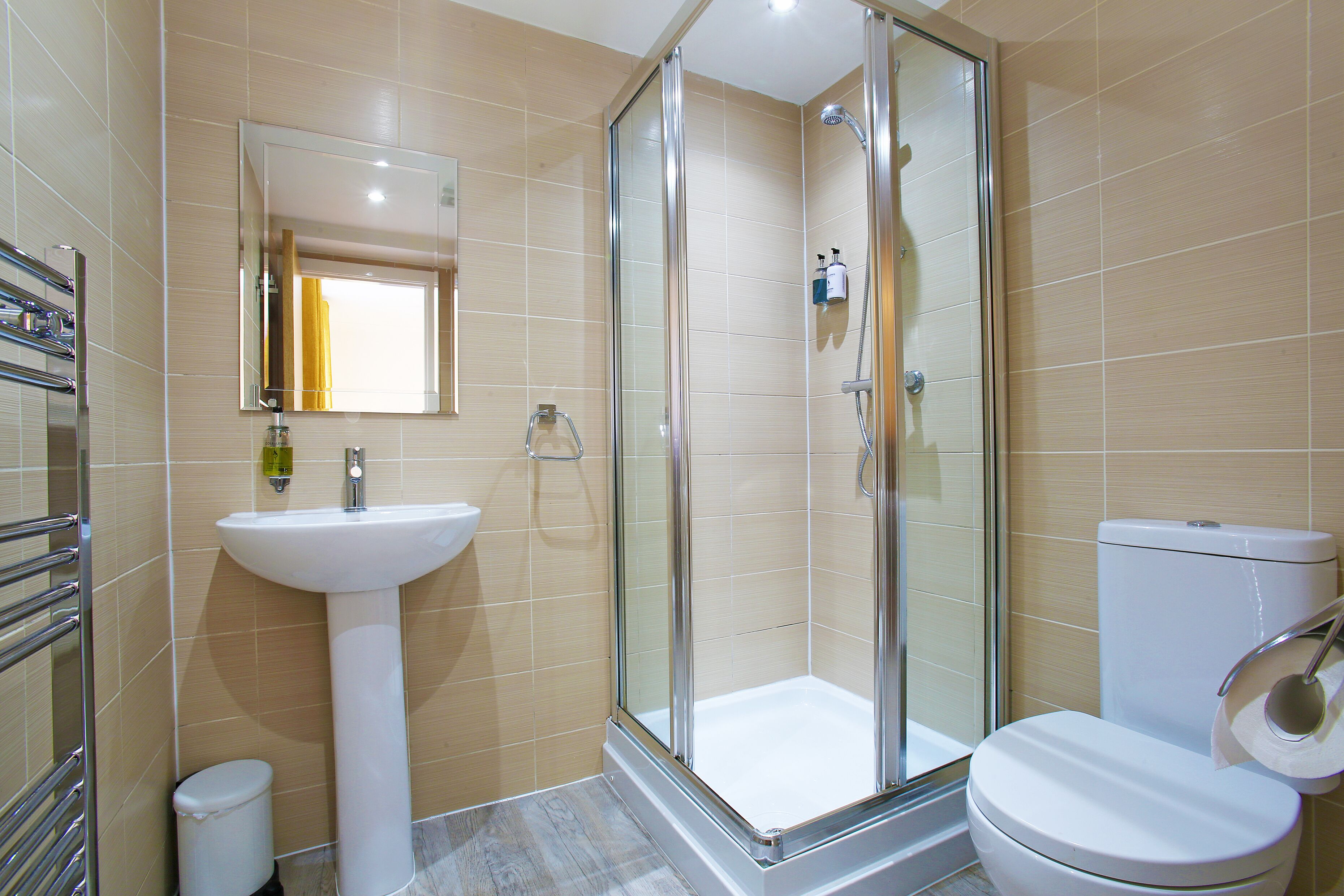 A modern bathroom with a glass-enclosed shower, a pedestal sink, and a toilet.