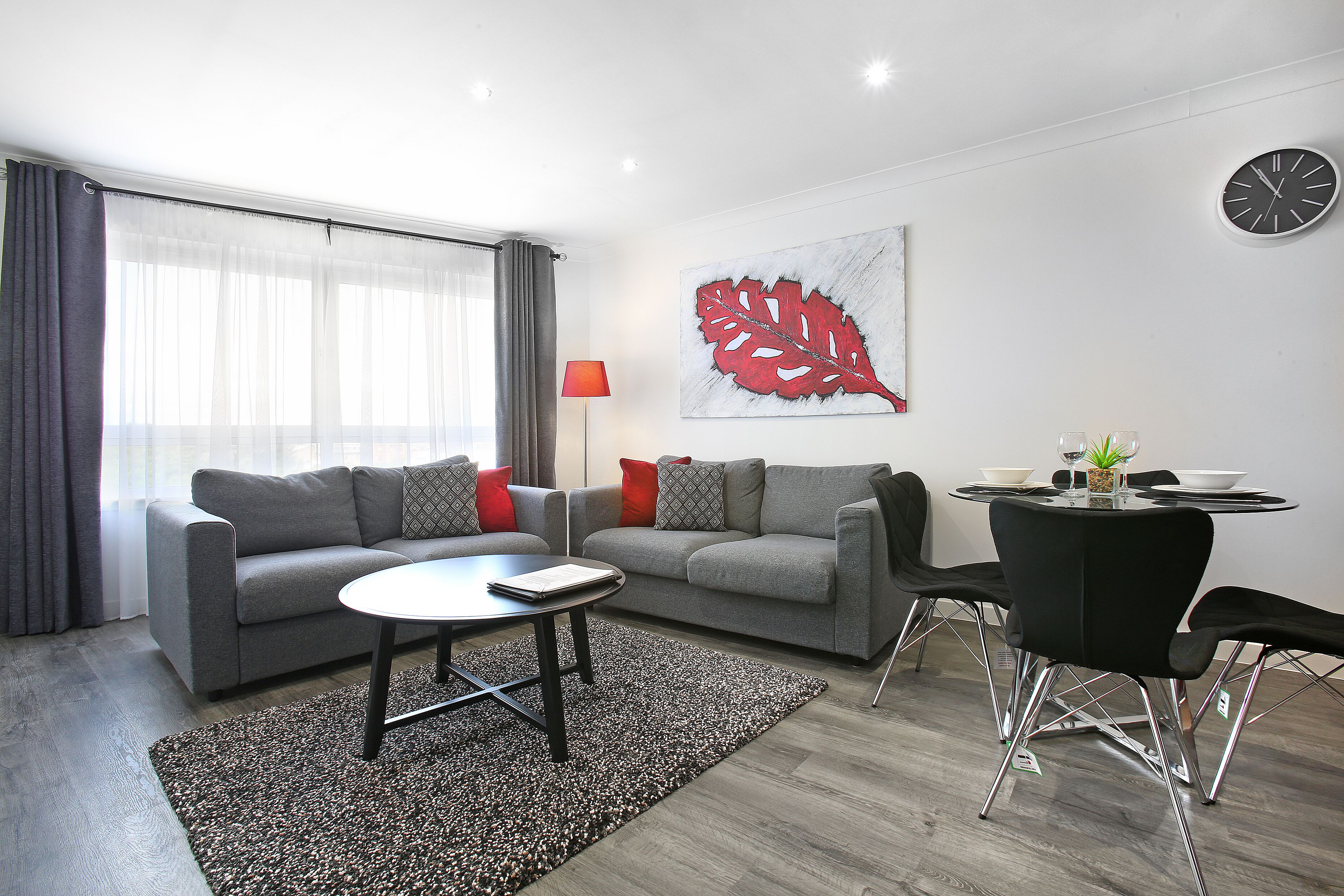 A modern living room with two grey sofas, a round coffee table, and a dining table with chairs.