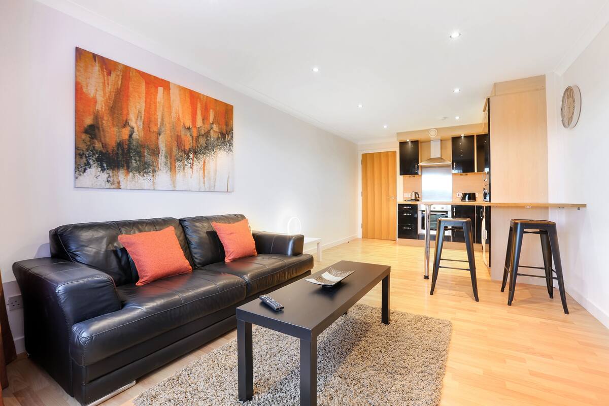 A modern living room with a black leather sofa, a coffee table, and a large abstract painting on the wall.