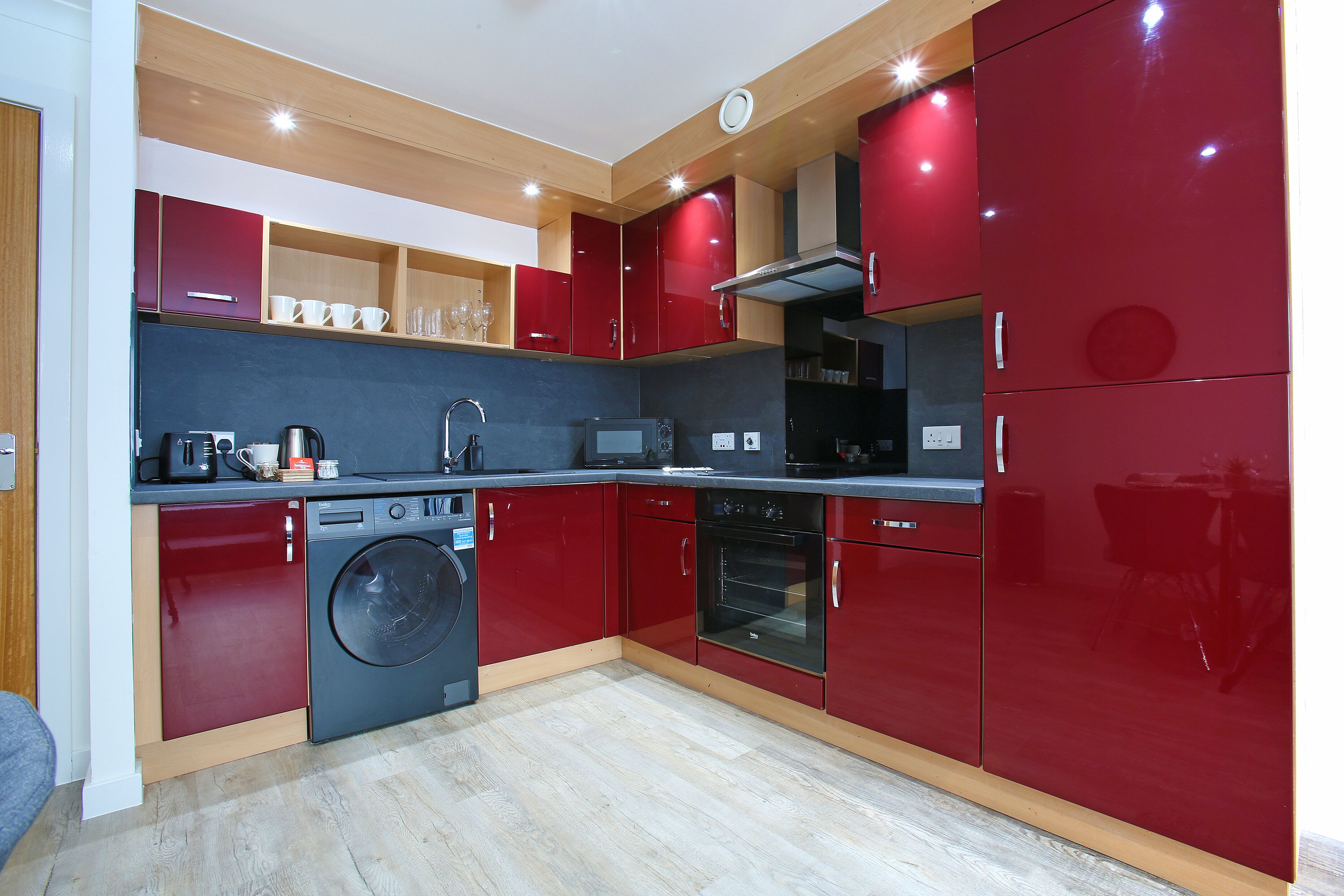 A compact kitchen with red cabinets, a washing machine, and a microwave.