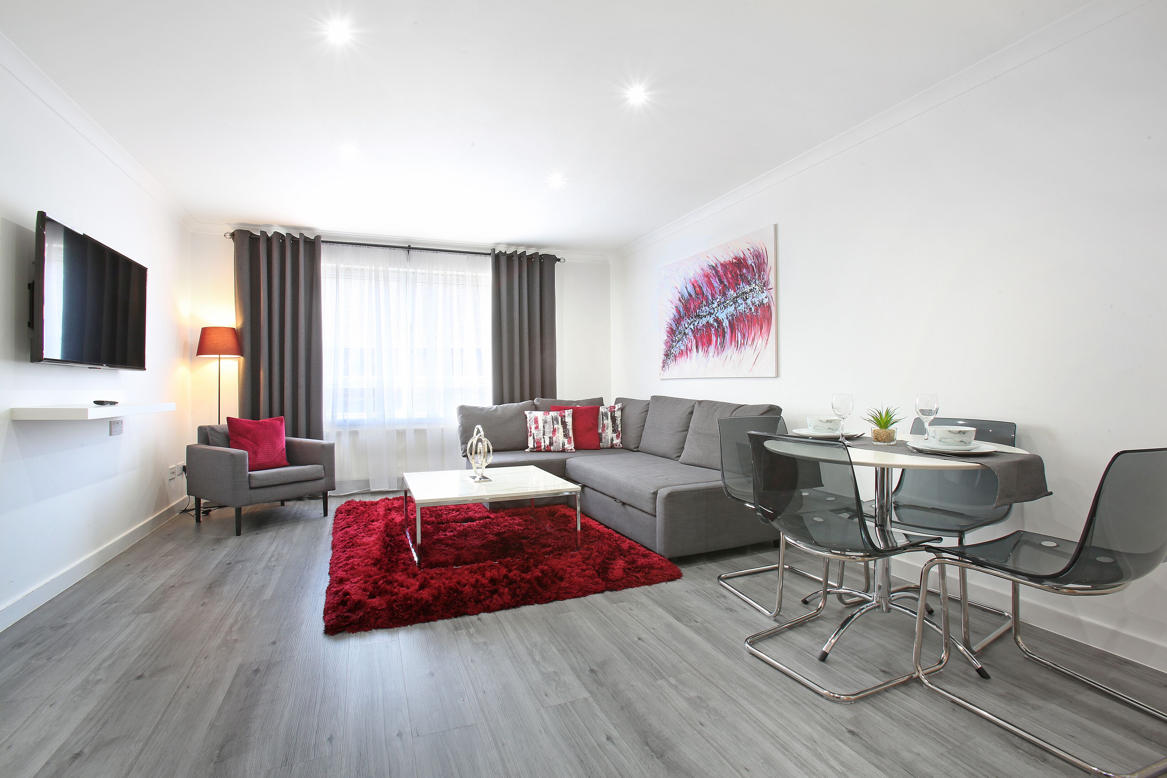 A modern living room with a grey sofa, red rug, and a dining area with a table and chairs.