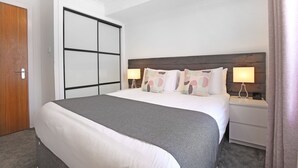 Een net opgemaakt bed met een grijze deken, een houten hoofdbord en twee bedlampjes.