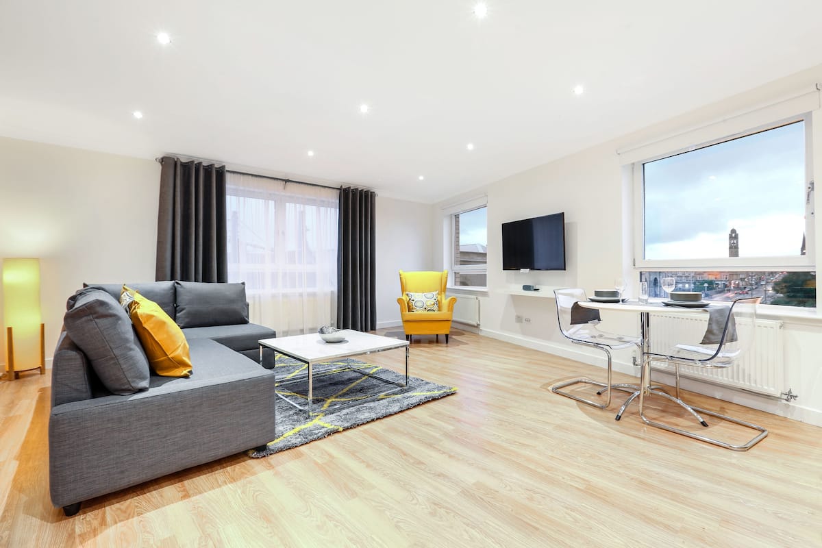 A modern living room with a grey sofa, yellow armchair, and a dining area with a table and chairs.